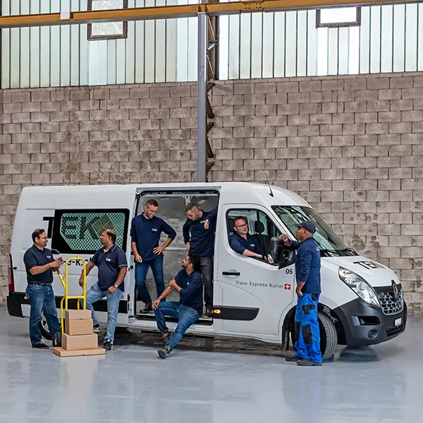 Mitarbeitende eines Handwerksbetriebs stehen und sitzen gemeinsam rund um ein Servicefahrzeug in einer Werkhalle.