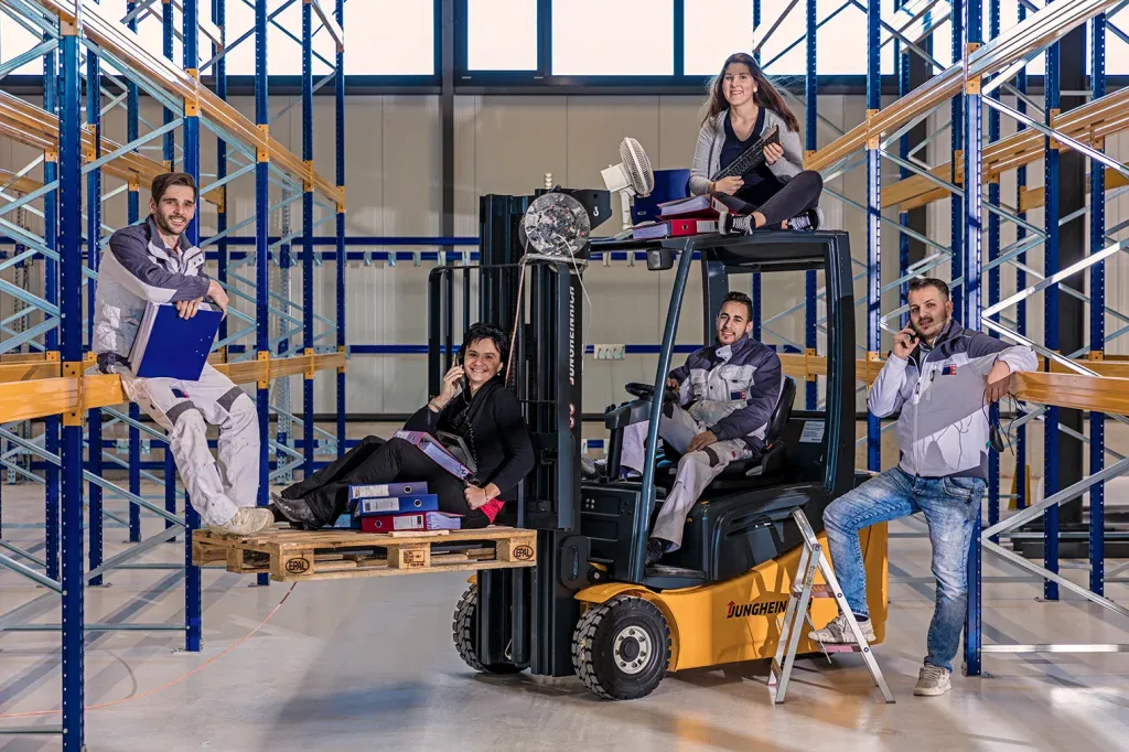 Dynamisches Teamfoto von Mitarbeitenden in einer Lagerhalle mit Stapler, passend für Teamseite und Unternehmensdarstellung.