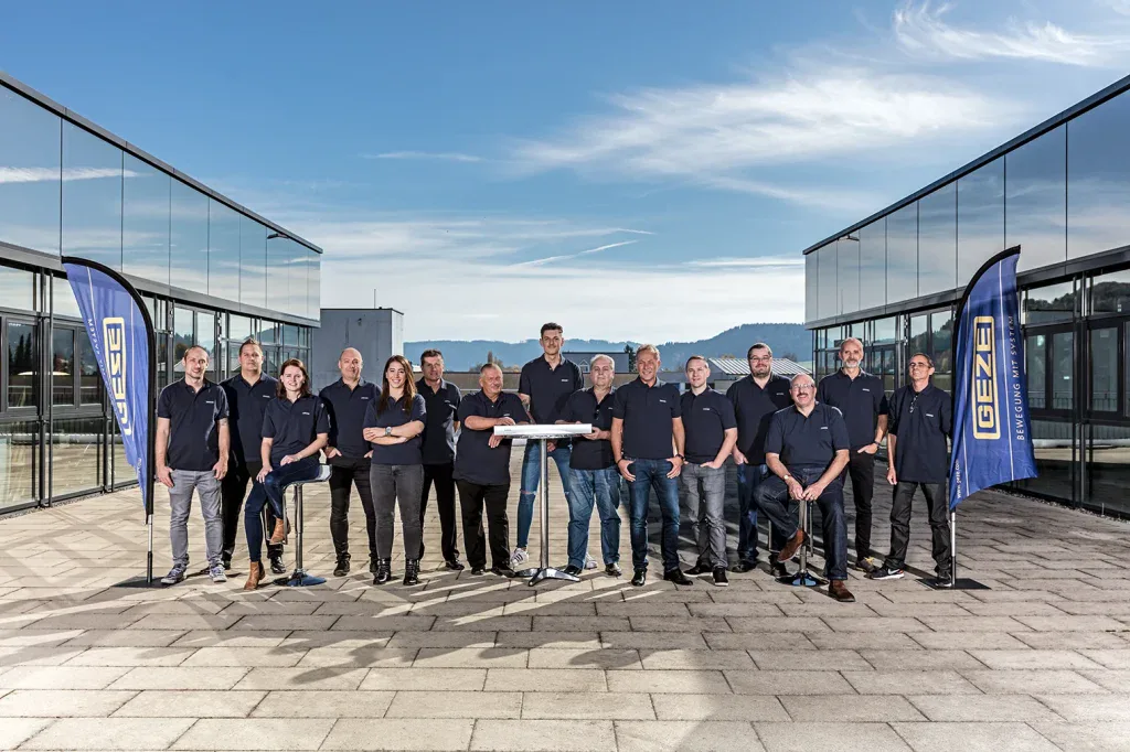 Grosses Teamfoto eines Unternehmens im Aussenbereich mit Firmengebäude im Hintergrund für Teamseite und Employer Branding.