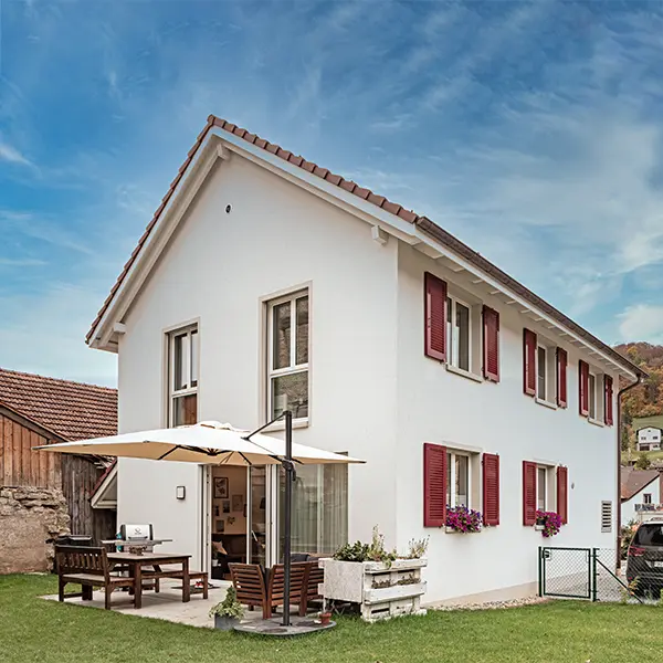 Weisses Einfamilienhaus mit roten Fensterläden und Sitzplatz im Garten